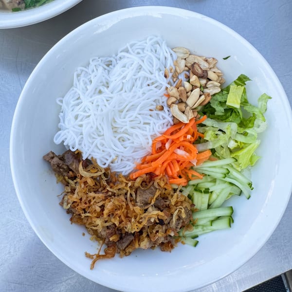 A white bowl of Vietnamese vermicelli noodles with beef, fried onions, peanuts, and fresh vegetables.