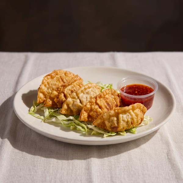 Crispy fried dumplings on a bed of shredded lettuce with a side of sweet chili sauce.